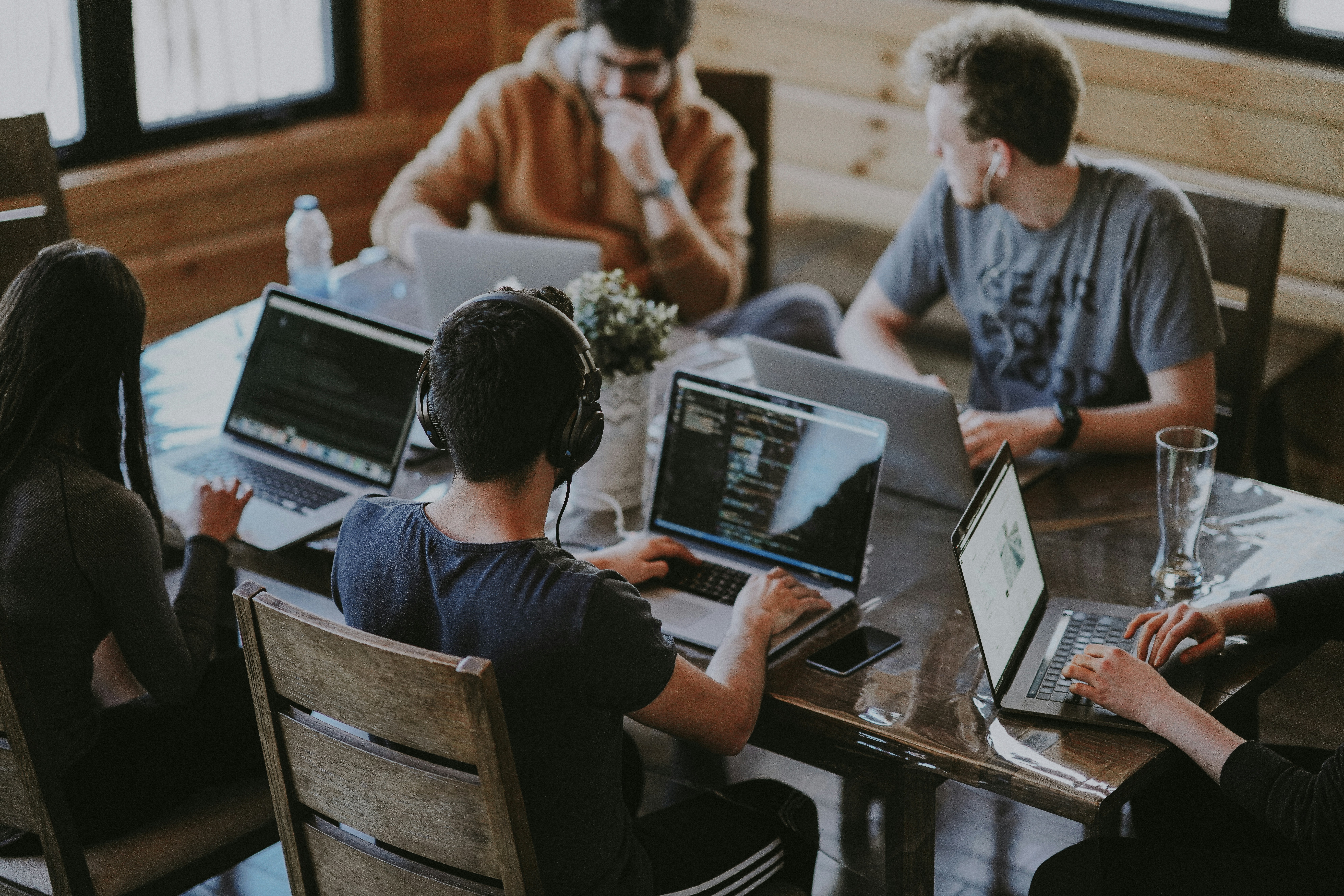 Five people are seated at a table, each with laptops in front of them as they work.